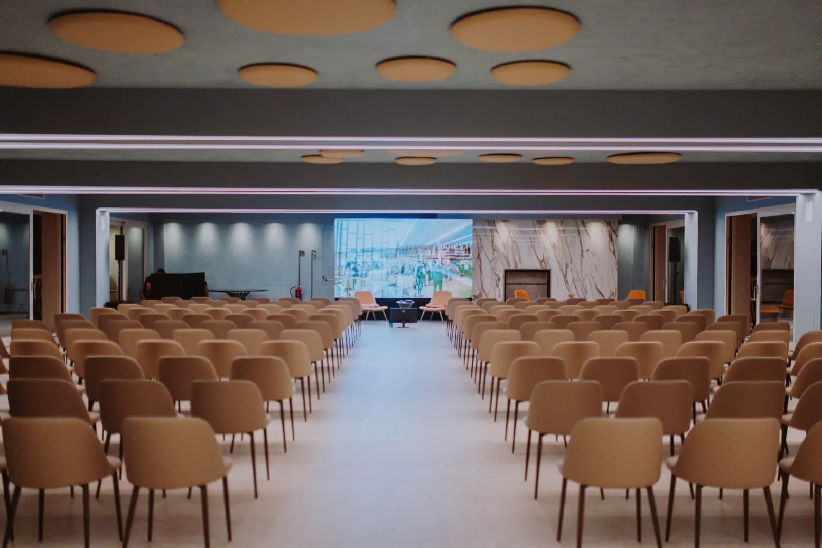 La sala allestita per una conferenza, vista dal corridoio centrale verso il palco e lo schermo